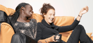 two women laughing together on a couch.
